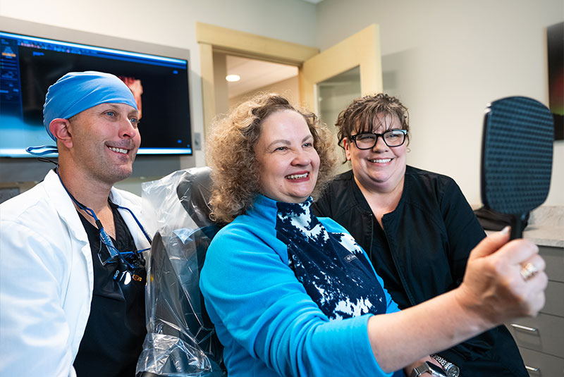 dental patient smiling brightly with doctor and staff member after patient's procedure